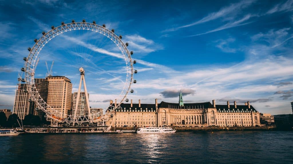 Ruota panoramica di Londra sul Tamigi con il edificio storico e il cielo sereno in background, icona turistica e attrazione della capitale britannica.