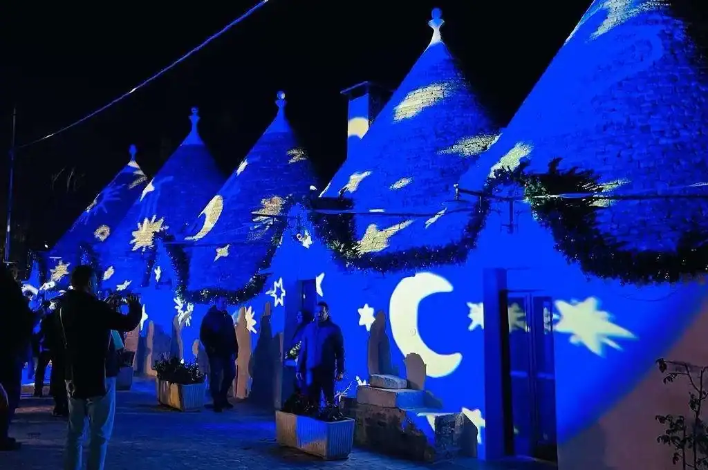 Suggestive lighting di luci blu proiezioni di stelle e lune su tetto di trulli in notturna, evento culturale o decorativo, atmosfera magica e suggestiva, tradizione e innovazione nel design.